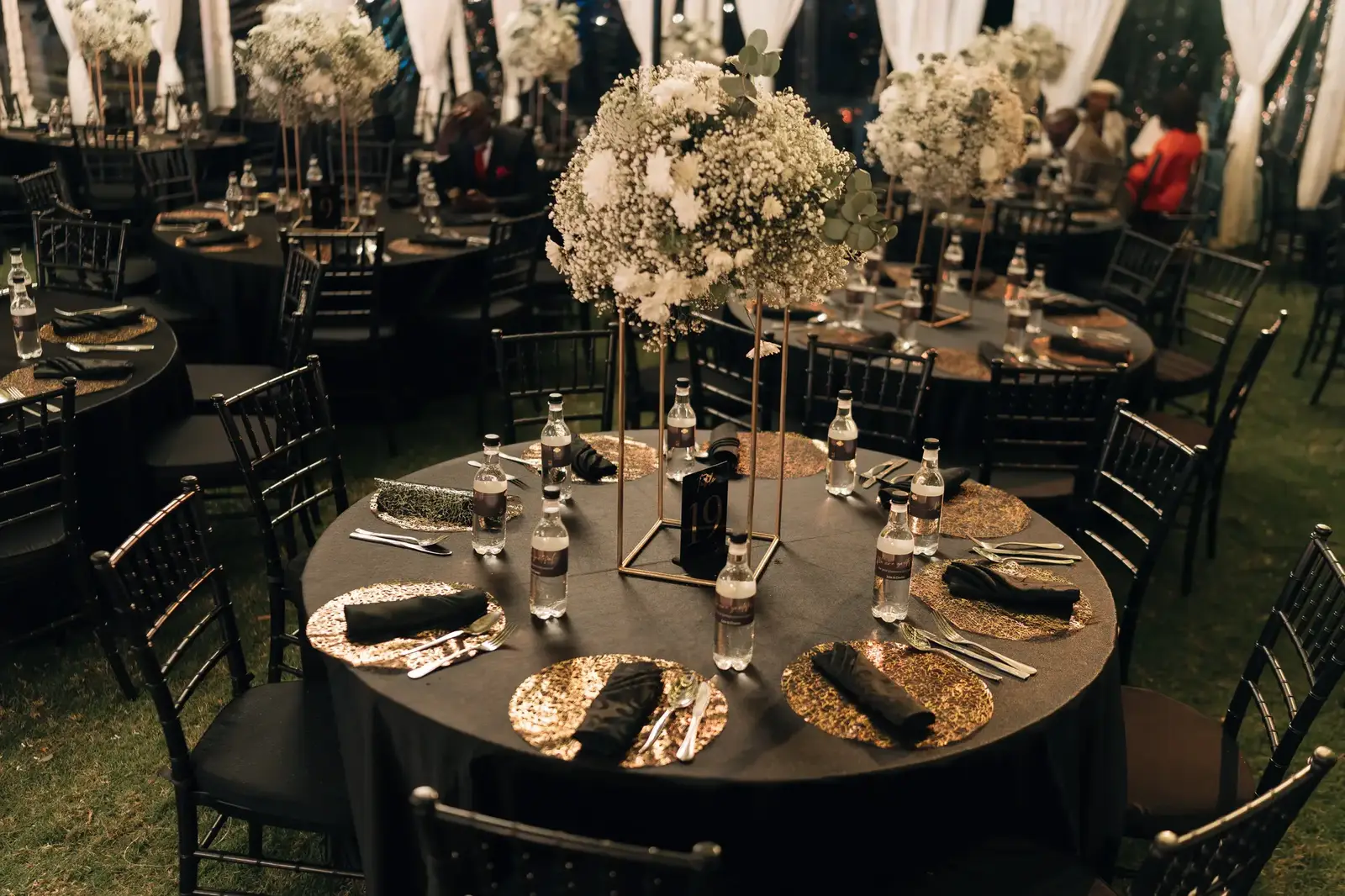 High-angle view of a black-themed table setting with gold sequin mats, black napkins, and a tall