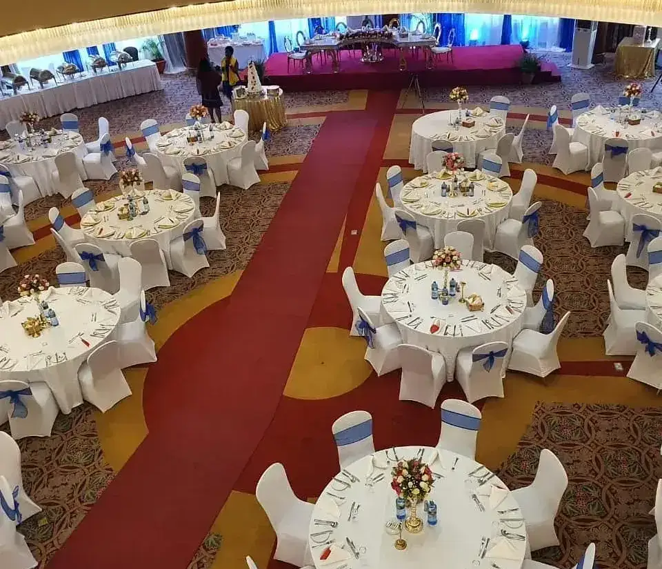 An indoor event hall with a red carpet aisle, white round tables, and a main stage with red drapes.
