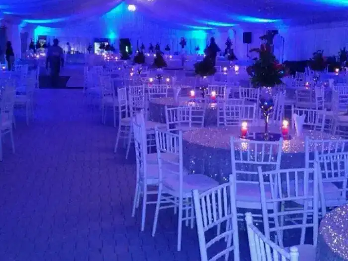 Large event hall with blue lighting and round tables with silver linens.