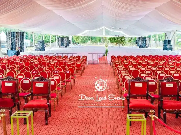 Grand tent interior with a red carpet aisle and rows of white chairs facing a stage.