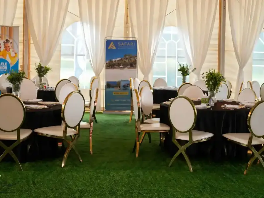 Elegant tent interior with black round tables, white gold-leg chairs, and white draped walls, with
