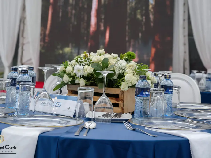 Eye-level view of a table setting focusing on the white floral centerpiece and a "Reserved" sign, with a forest backdrop screen.