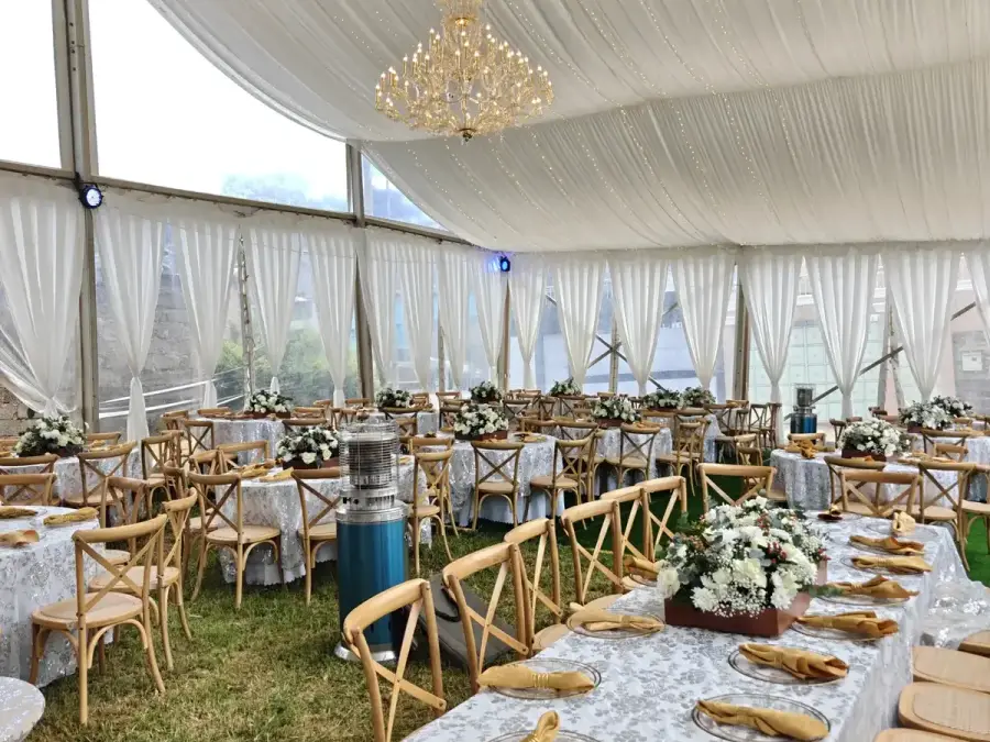 Interior of a white marquee tent with draped ceilings, a crystal chandelier, and round tables with