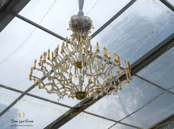Large, intricate crystal chandelier hanging from the ceiling structure of an event tent.