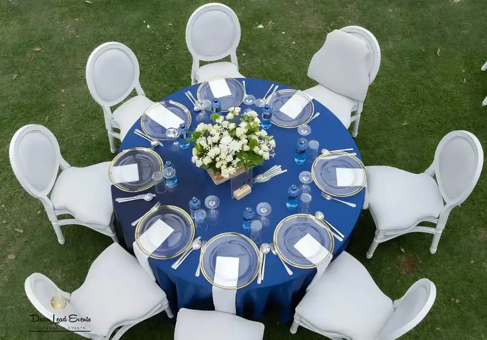 Aerial view of a round table set up with a navy blue tablecloth, gold-rimmed clear glass chargers