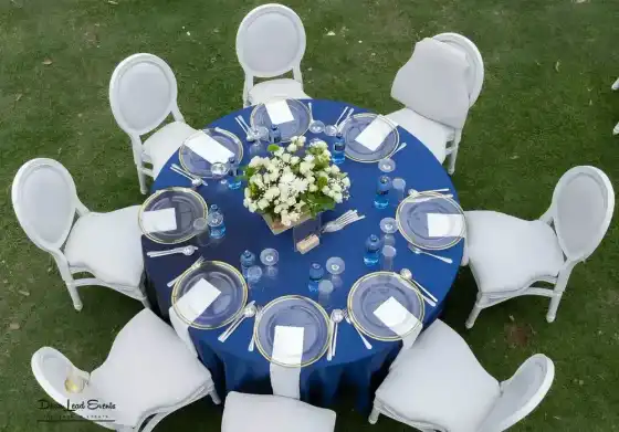 Aerial view of a round table set up with a navy blue tablecloth, gold-rimmed clear glass chargers