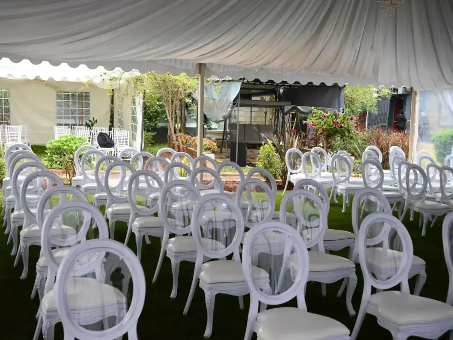 Rows of white Louis chairs arranged on a grassy lawn under a white marquee tent for an audience or