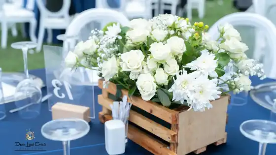 Close-up of a white rose floral arrangement in a rustic wooden crate on a blue tablecloth, with
