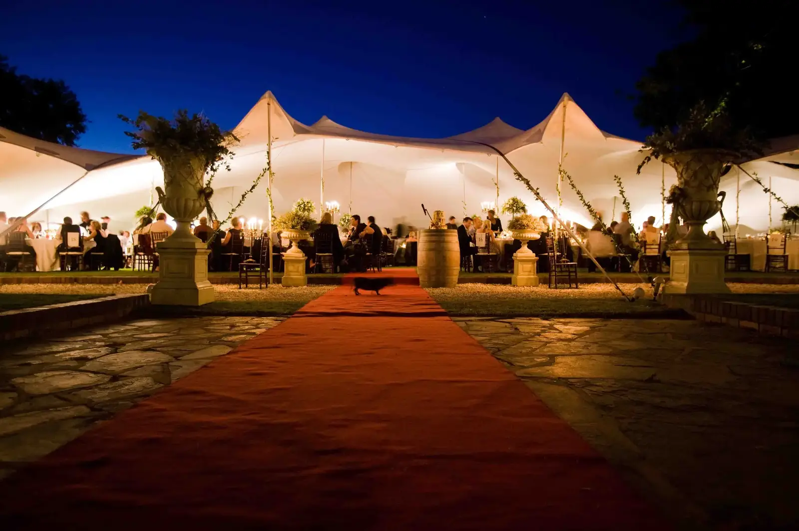 Nighttime view of a white stretch tent with a red carpet entrance, warm interior lighting, and